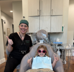 Dental team member and child in the dental chair both giving thumbs up