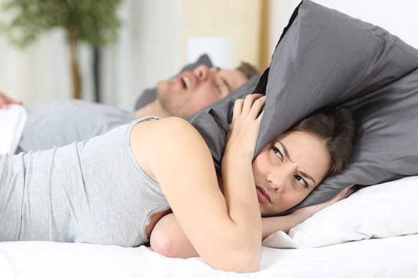 woman covering her ears with her pillows to block out her partner's excessive snoring