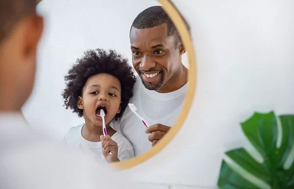 dad showing his kid how to brush his teeth