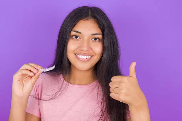 young teen girl giving a thumbs up with a SureSmile aligner in her other hand